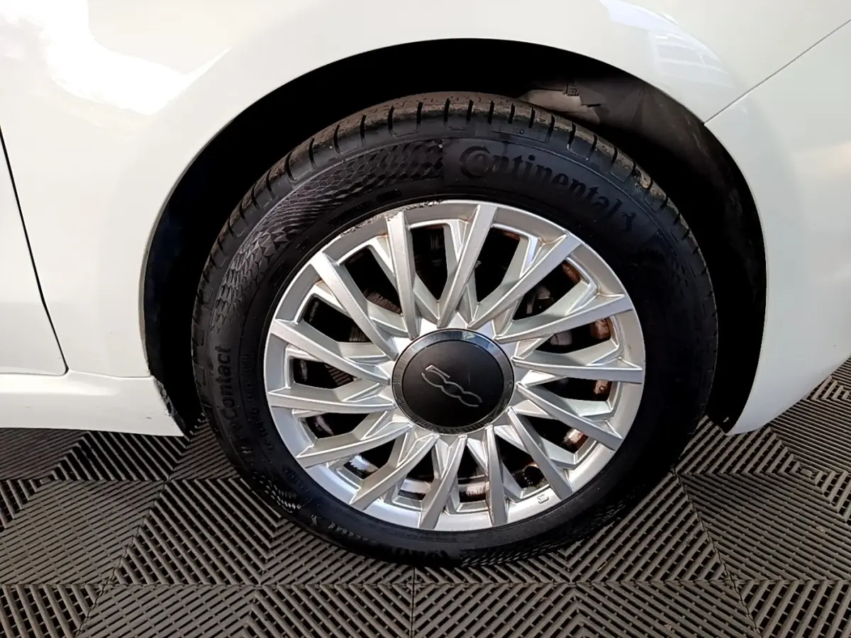 Gros plan sur la roue avant droite blanche d'une FIAT 500 Dolcevita avec jante argentée à motifs rayonnants.