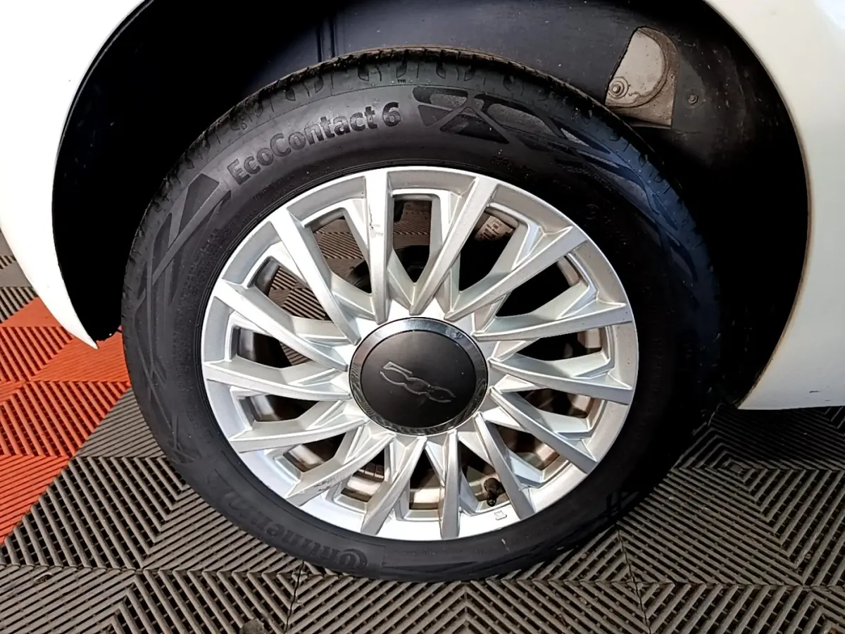 Gros plan sur la roue avant droite d'une FIAT 500 blanche avec jante alliage au design étoilé.