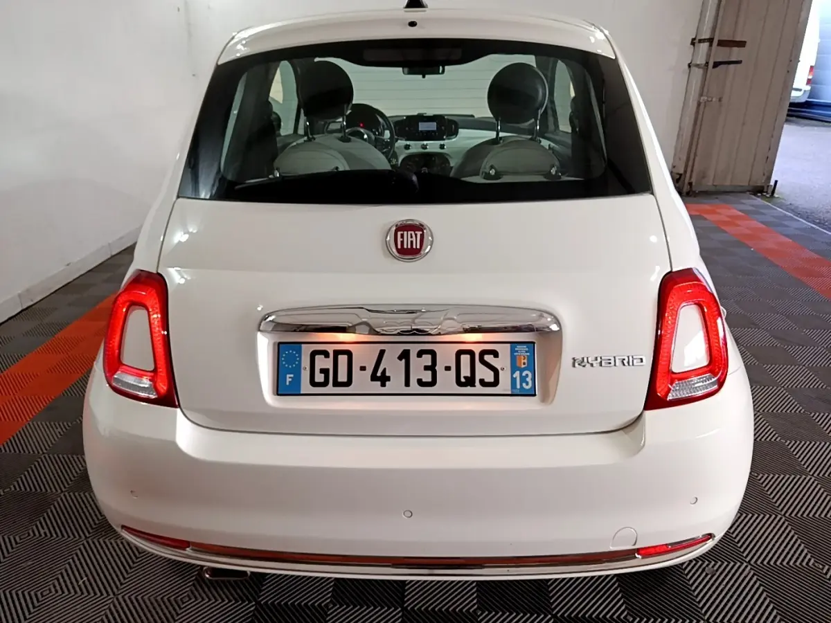 Vue arrière d'une FIAT 500 blanche hybride, avec feux arrière allumés et logo "Hybrid" visible à droite.