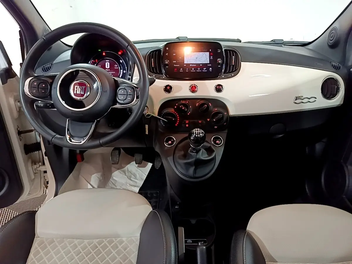 Vue intérieure avant de la Fiat 500 Hybrid blanche, tableau de bord avec écran tactile et volant multifonctions cuir.