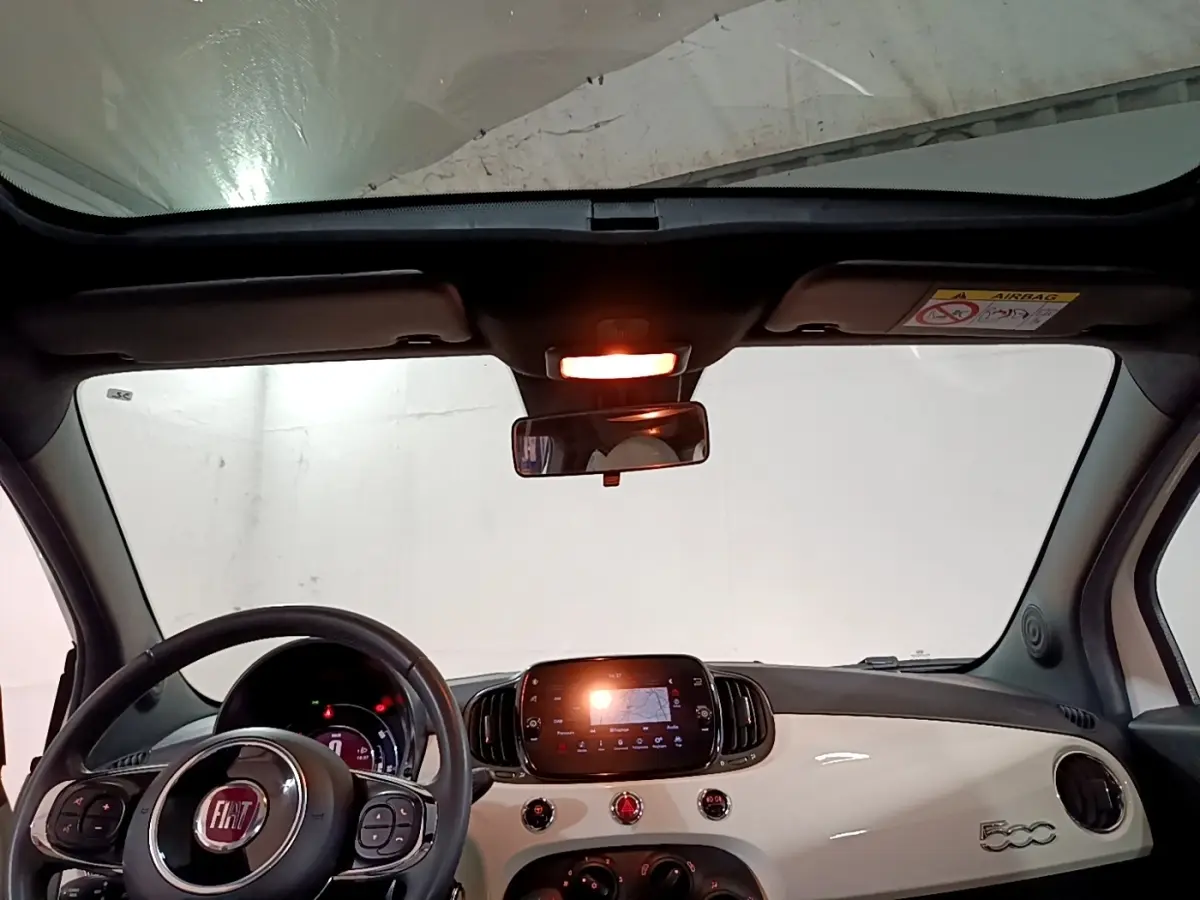 Vue intérieure avant de la Fiat 500 Hybrid blanche, avec tableau de bord brillant et écran tactile central allumé.