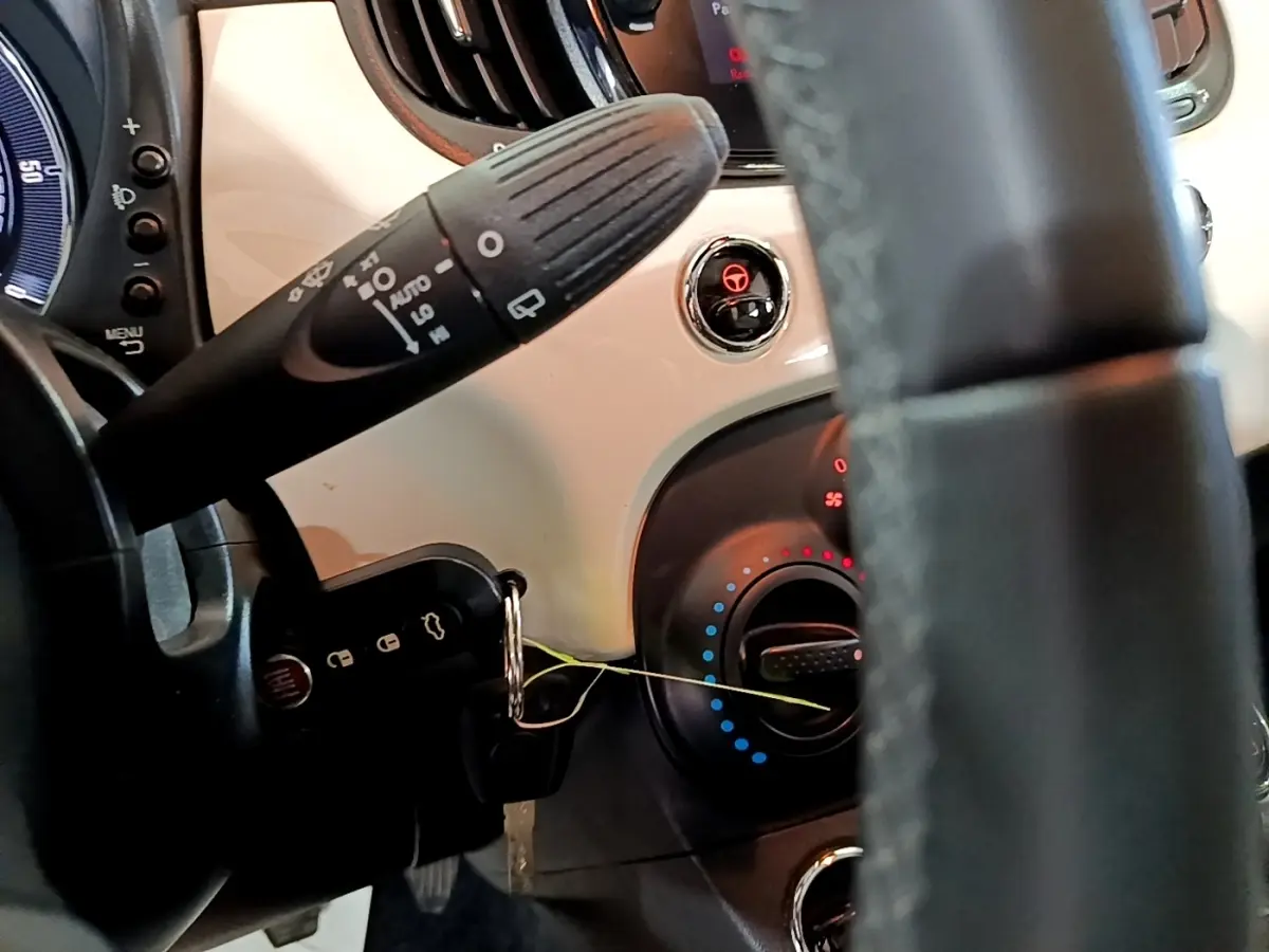 Gros plan sur le tableau de bord blanc et le volant noir de la Fiat 500 Hybrid, avec commandes et clé insérée.