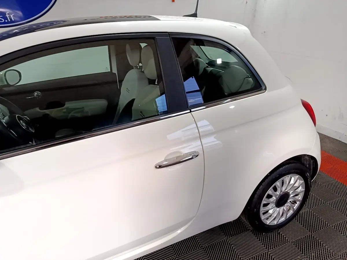 Vue latérale droite d'une Fiat 500 blanche avec jantes argentées et intérieur clair visible.