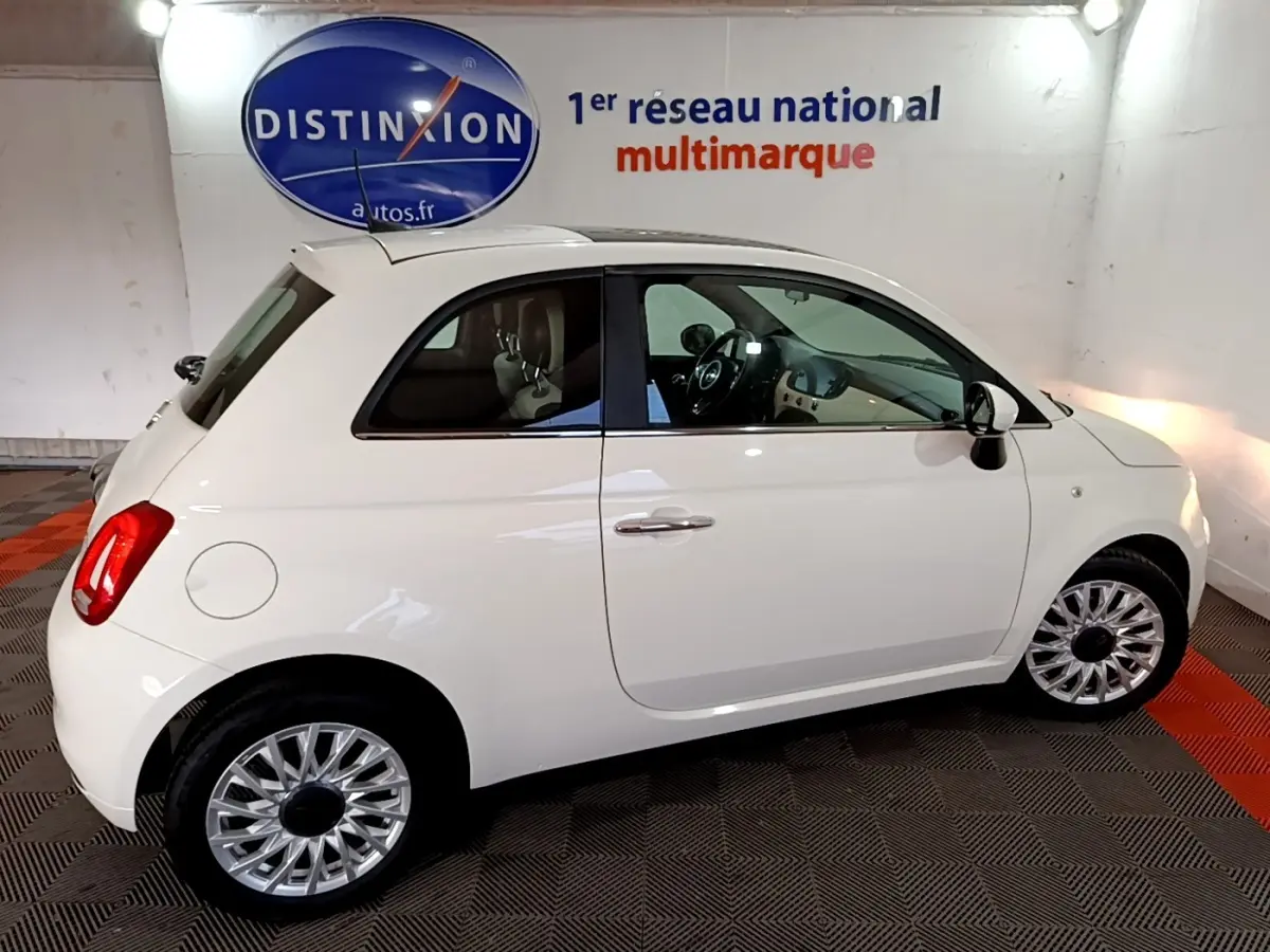 Profil droit d'une FIAT 500 blanche hybride 2021 stationnée en intérieur avec jantes argentées et toit blanc.