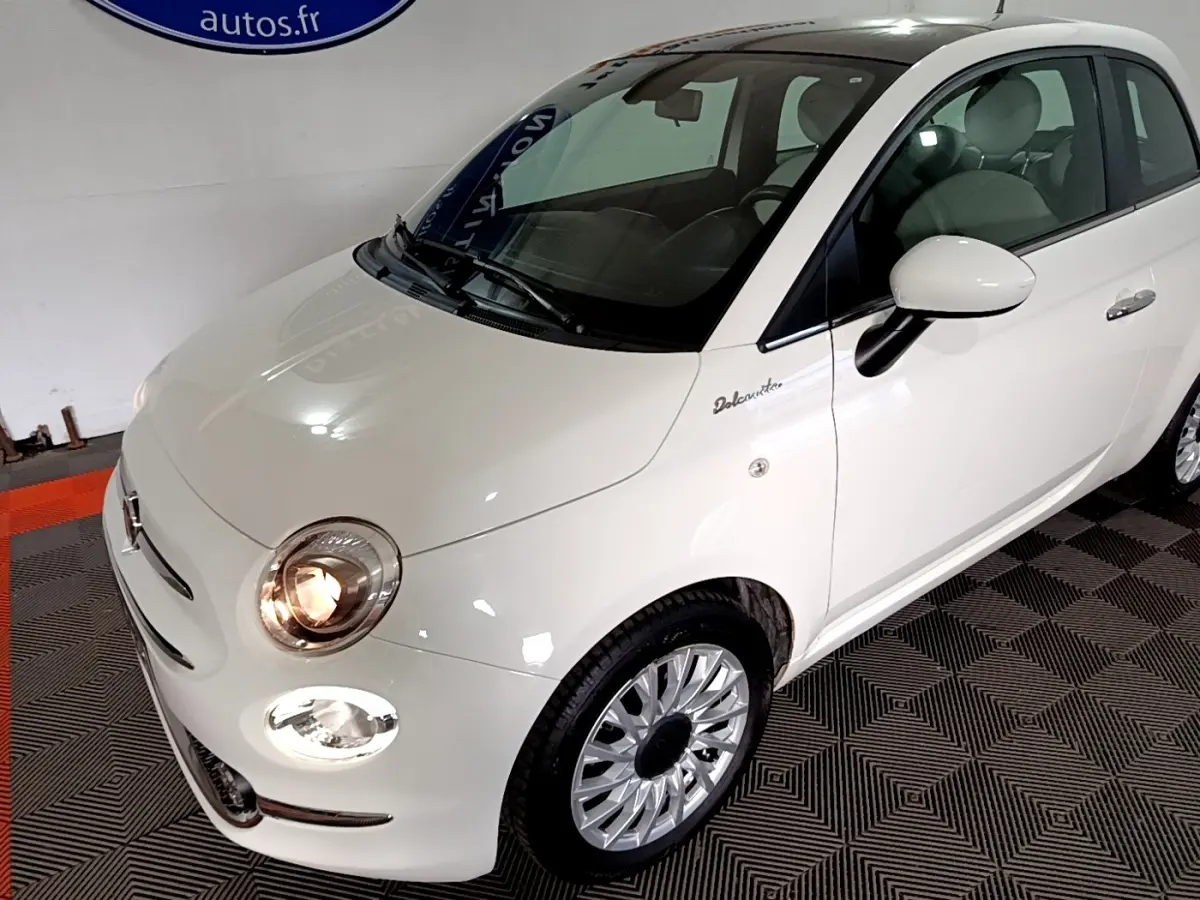 Vue 3/4 avant droite de la Fiat 500 Dolcevita blanche avec phares allumés et jantes alliage distinctives.