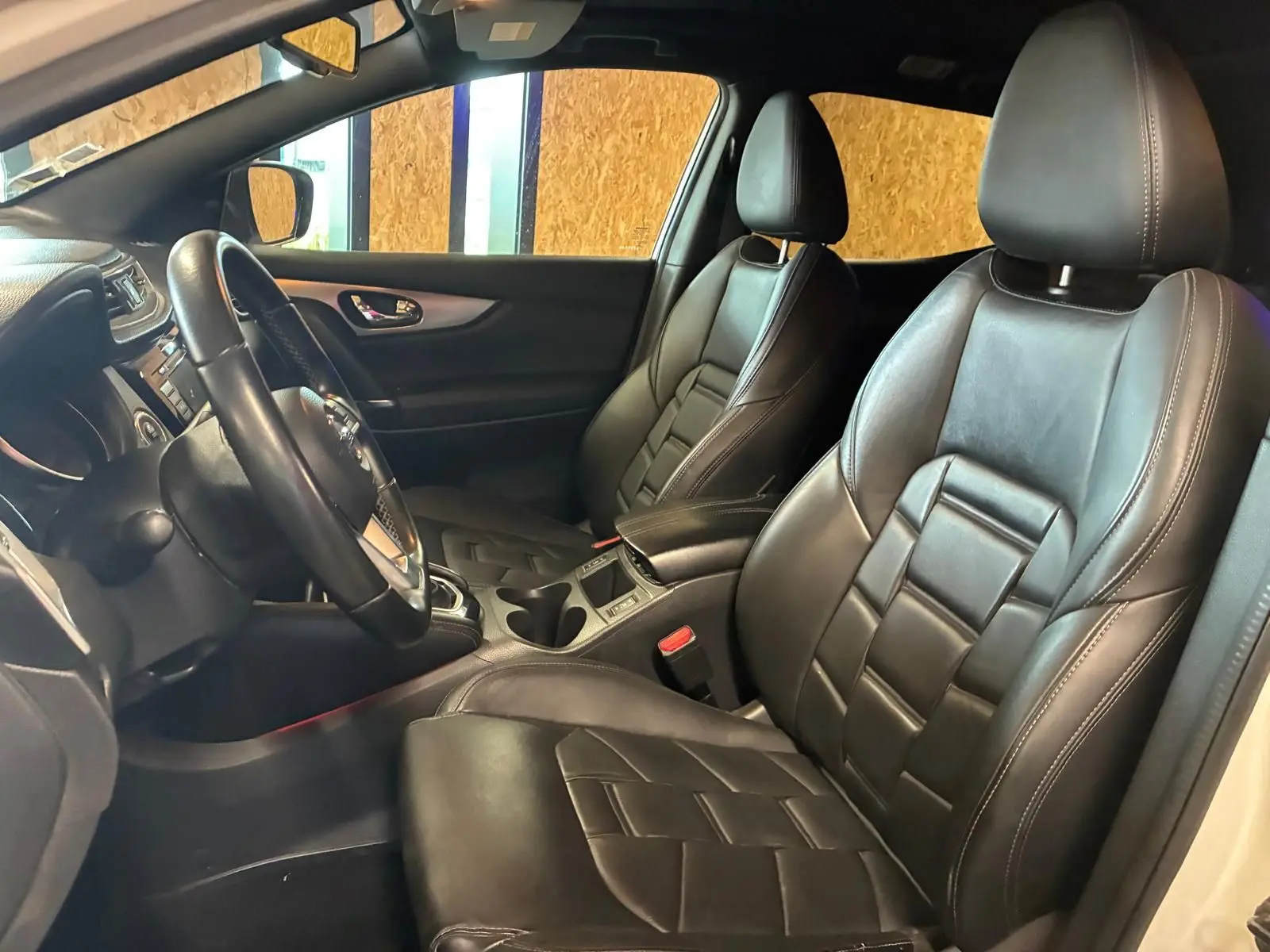 Vue intérieure côté conducteur du Nissan Qashqai blanc 2021, sièges en cuir noir et volant multifonction.