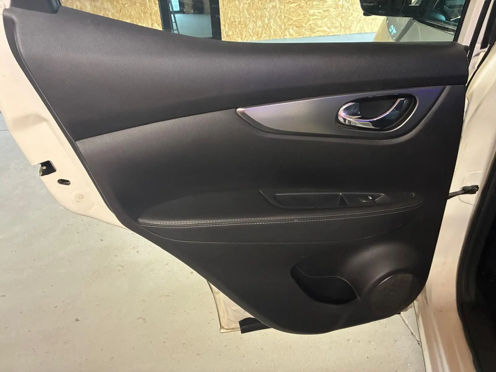 Gros plan sur la porte arrière droite noire en cuir du Nissan Qashqai blanc 2021, avec poignée chromée et bouton de fenêtre.