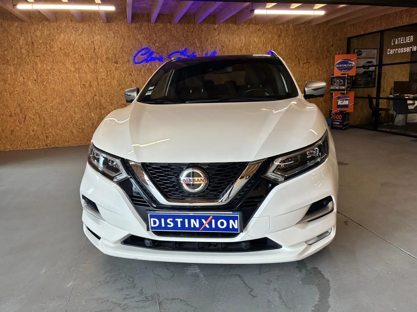 Vue frontale d'un Nissan Qashqai blanc 2021 dans un showroom avec logo Distinxion sur la plaque avant.