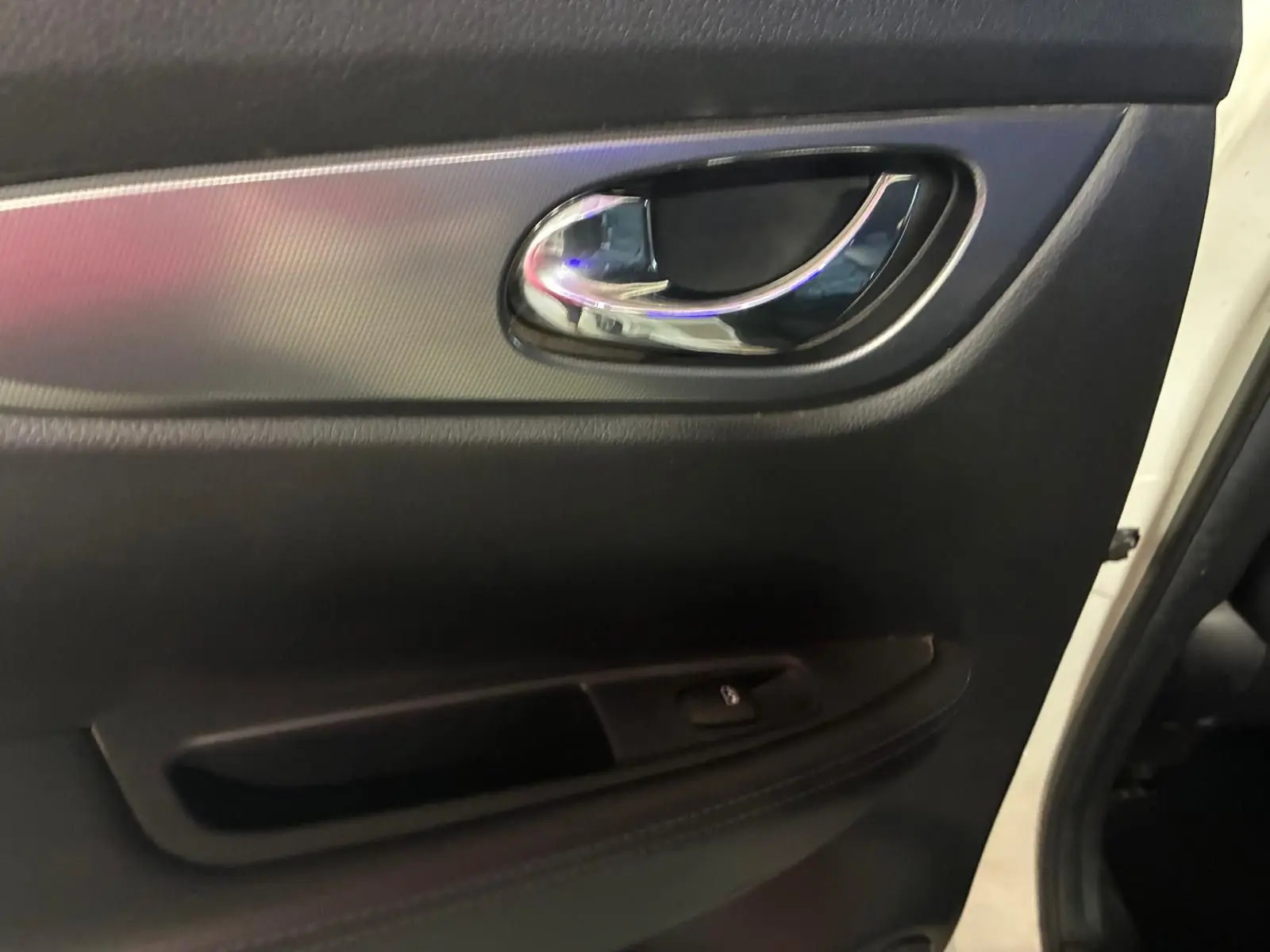 Poignée de porte intérieure côté gauche du Nissan Qashqai blanc 2021, avec finition noire et insert chromé.