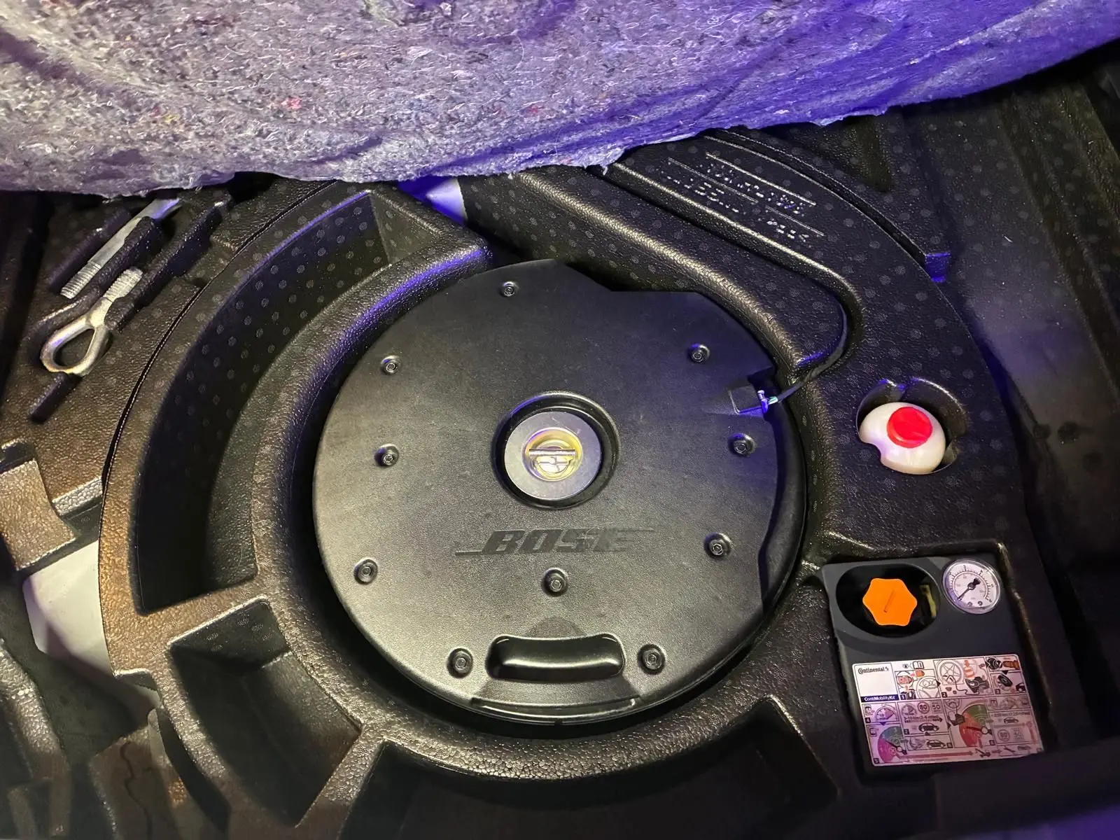 Détail du coffre du Nissan Qashqai blanc 2021 montrant le caisson Bose intégré et les outils de secours.