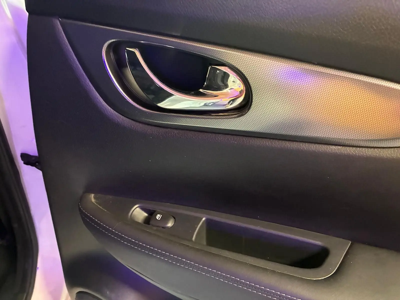 Gros plan sur la poignée intérieure chromée et le panneau de porte noir du Nissan Qashqai 1.5 BluedCi 2021 côté gauche.