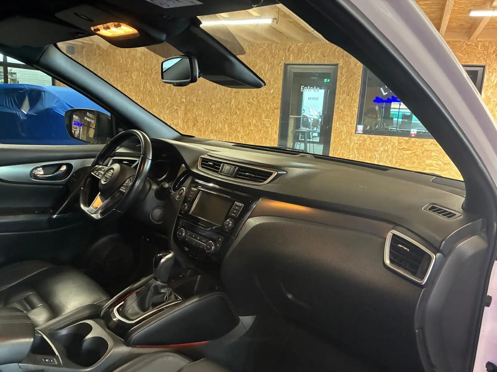 Vue intérieure côté conducteur du Nissan Qashqai blanc 2021, avec tableau de bord noir et sellerie cuir chauffante.