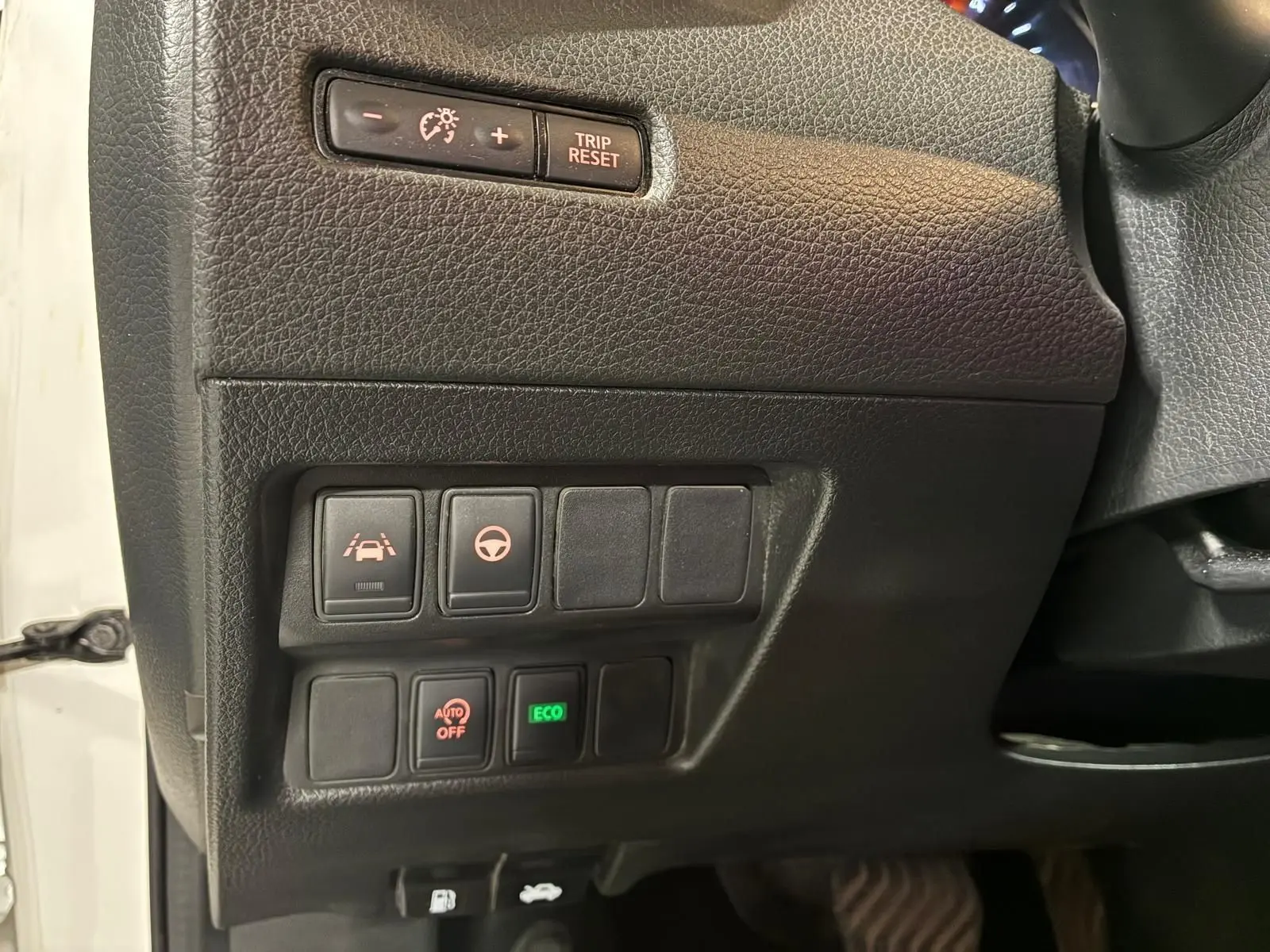 Détail des commandes côté gauche du tableau de bord noir du Nissan Qashqai blanc, avec boutons d'assistance et mode ECO.