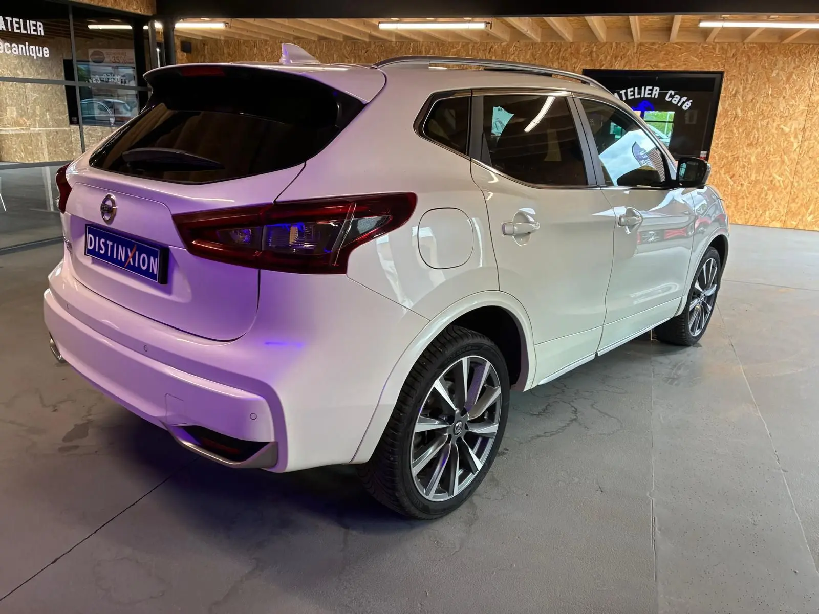 Vue 3/4 arrière droite d'un Nissan Qashqai blanc 2021 avec jantes alliage et vitres teintées, stationné en intérieur.