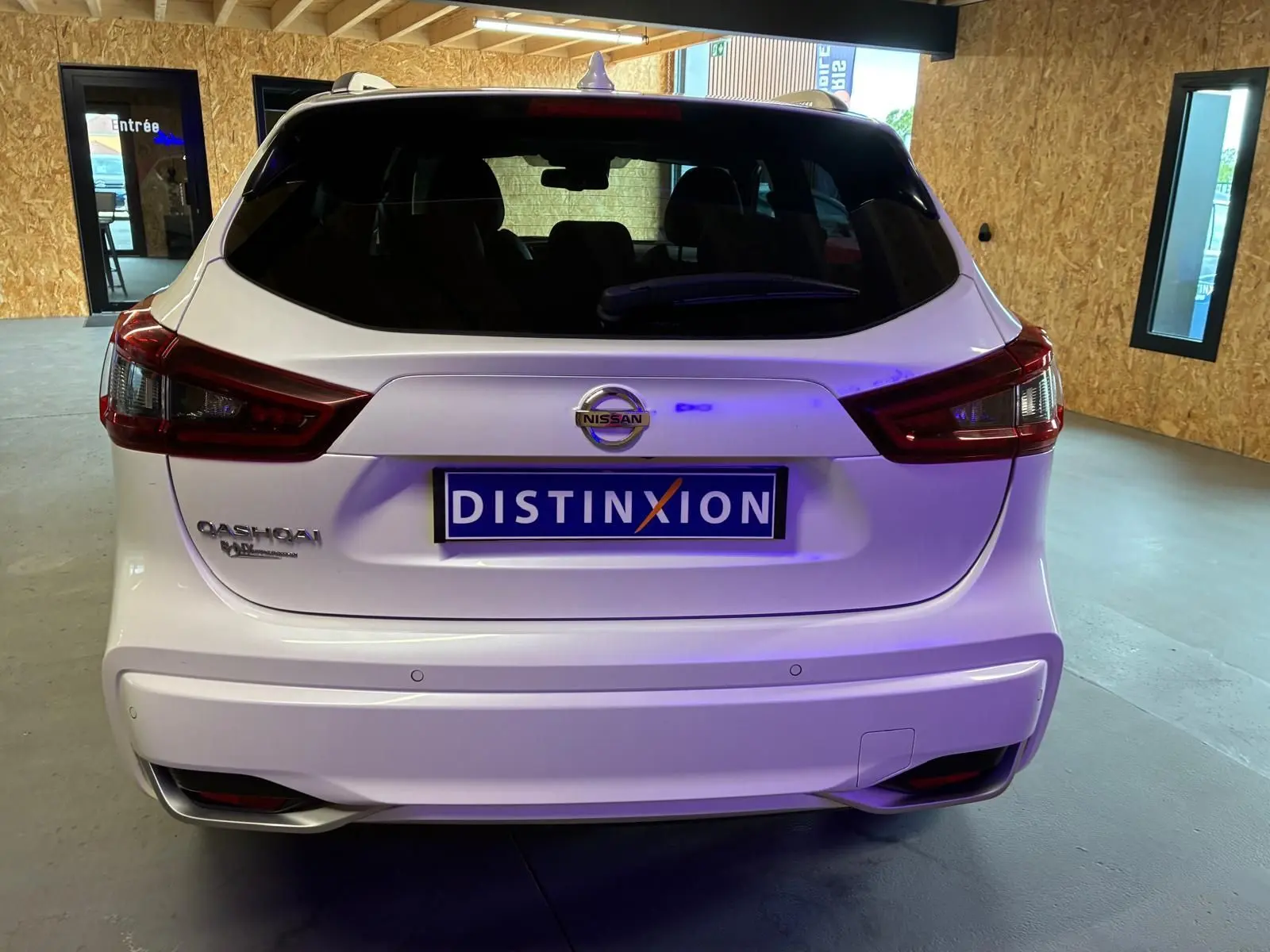 Vue arrière d'un Nissan Qashqai blanc 2021 avec logo et plaque Distinxion dans un garage lumineux.