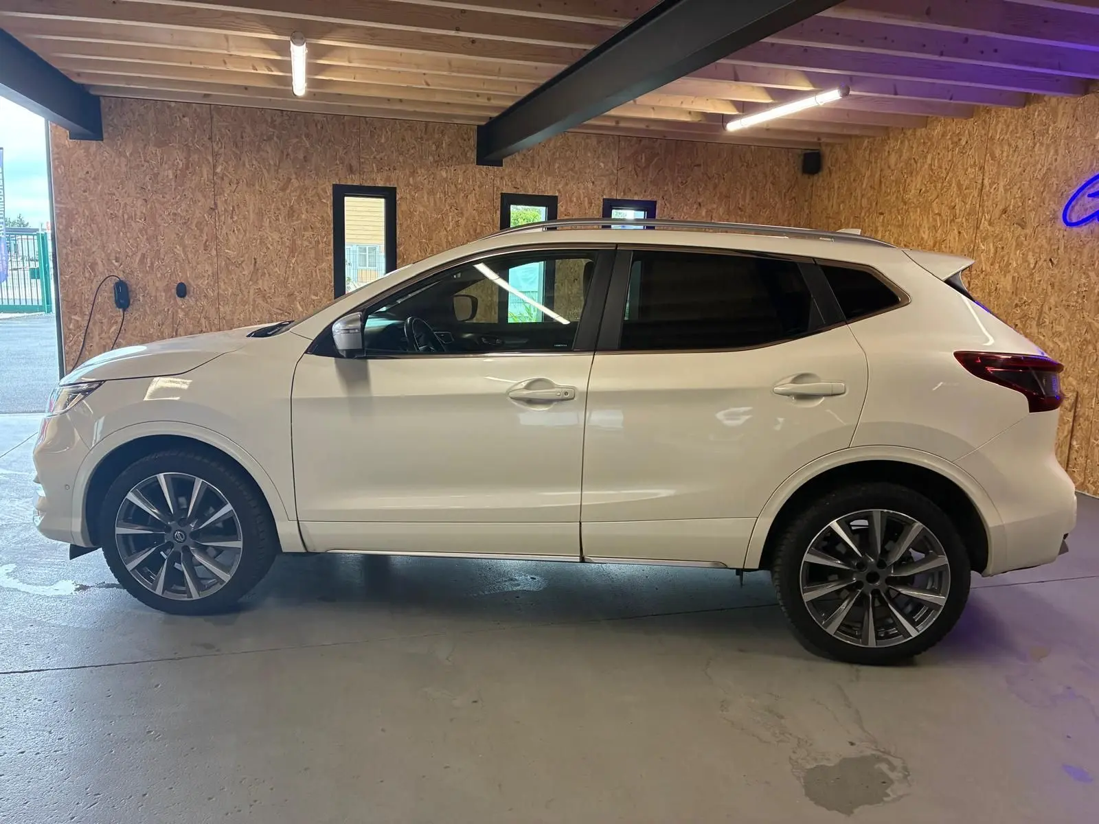 Vue de profil côté gauche d'un Nissan Qashqai blanc 2021 stationné en intérieur avec jantes alliage foncé.