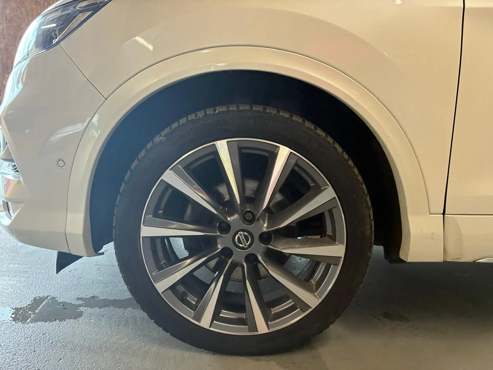 Gros plan sur la roue avant gauche d'un Nissan Qashqai blanc, mettant en valeur la jante alliage moderne.