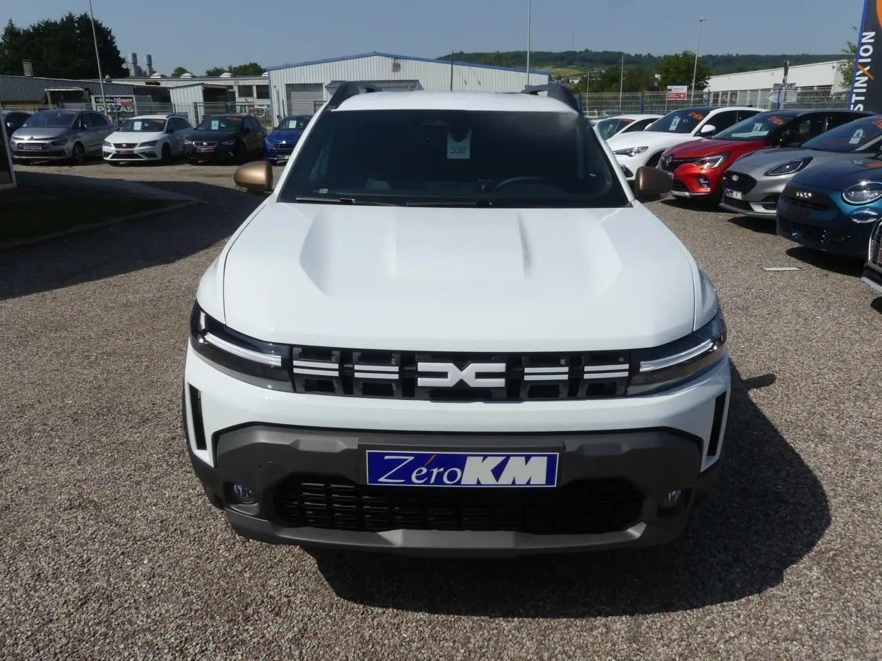 Vue de face d'un Dacia Duster blanc avec calandre noire et détails de bouclier gris foncé sur parking.