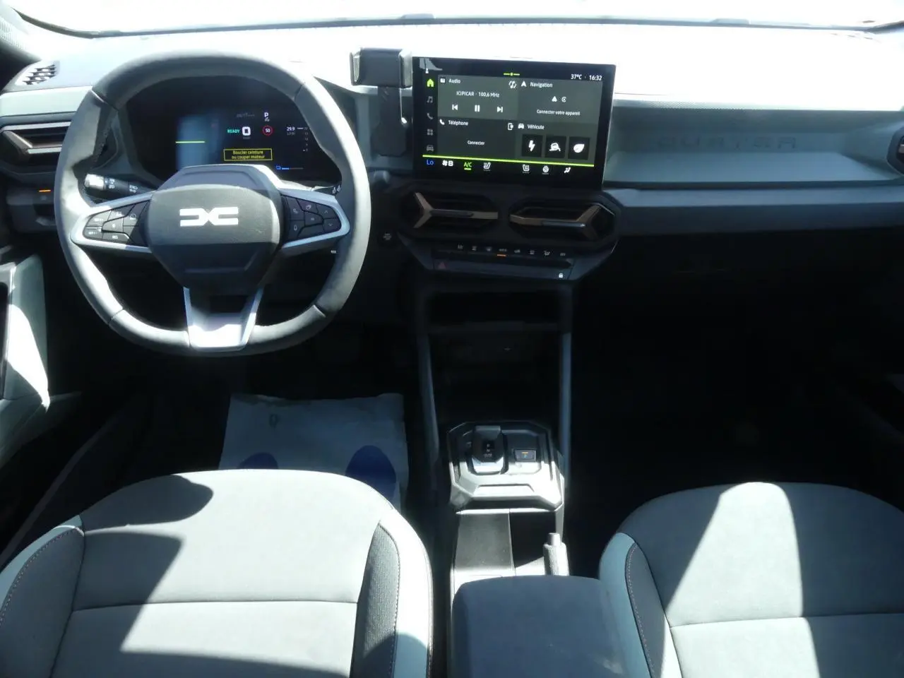 Intérieur du Dacia Duster 2025 en vue frontale, tableau de bord noir avec écran tactile central et volant multifonction.