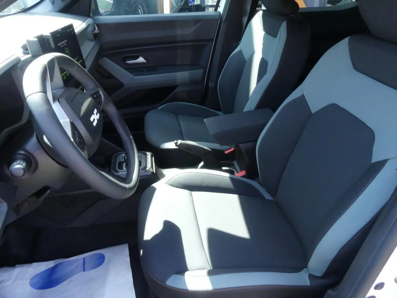 Intérieur avant droit du Dacia Duster 2025, sièges bi-ton gris avec accoudoir central et volant noir.
