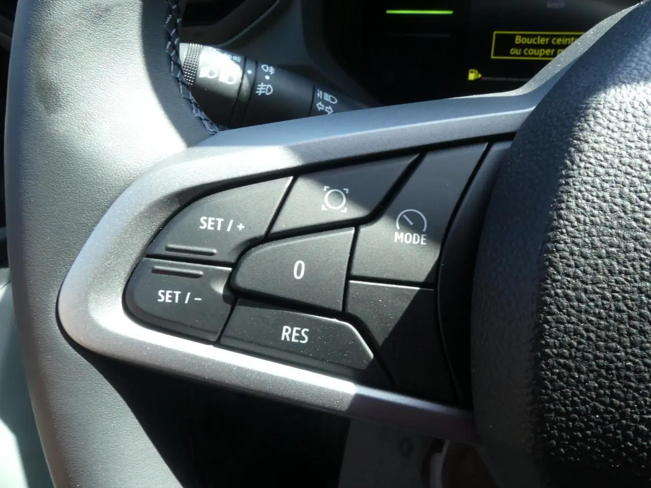 Gros plan sur les commandes de régulateur de vitesse au volant noir du Dacia Duster blanc hybride 2025.