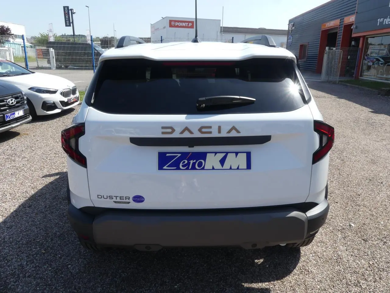 Vue arrière d'un Dacia Duster blanc avec logo brun cuivré et plaque d'immatriculation Zero KM visible.