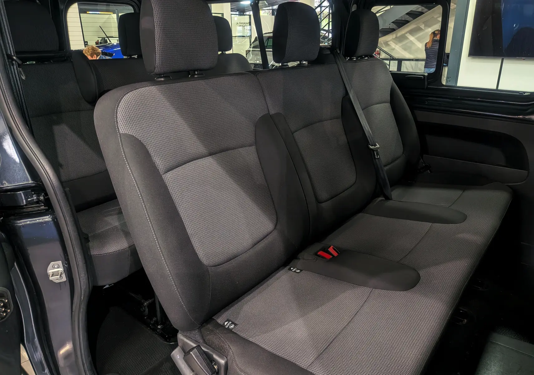 Vue intérieure du siège arrière en tissu gris foncé du Renault Trafic Combi L2 9 places, avec porte coulissante ouverte côté droit.