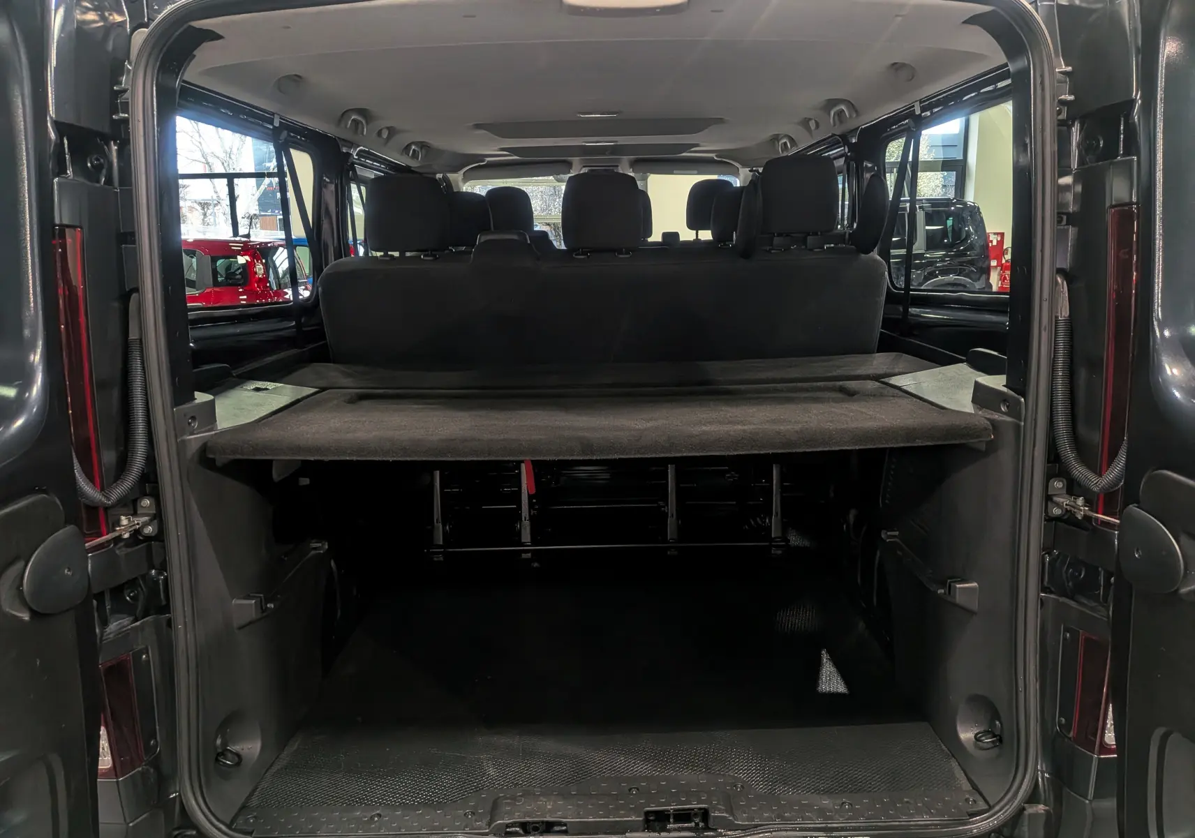 Vue arrière ouverte du Renault Trafic Combi gris Comète 2023, montrant l'espace de chargement et les sièges arrière en tissu noir.