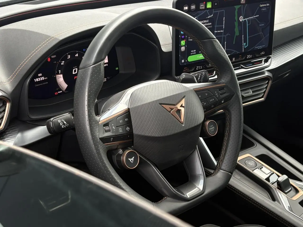 Vue rapprochée du volant cuir noir perforé avec logo CUPRA cuivré et tableau de bord digital du Leon 2025.