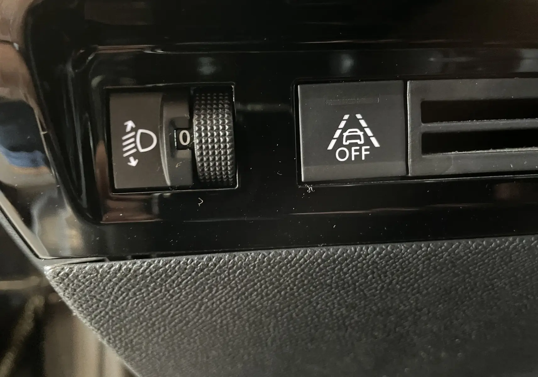 Détail intérieur du tableau de bord de la Peugeot 508 gris platinium, bouton de réglage des phares et désactivation de l'alerte de franchissement de ligne.