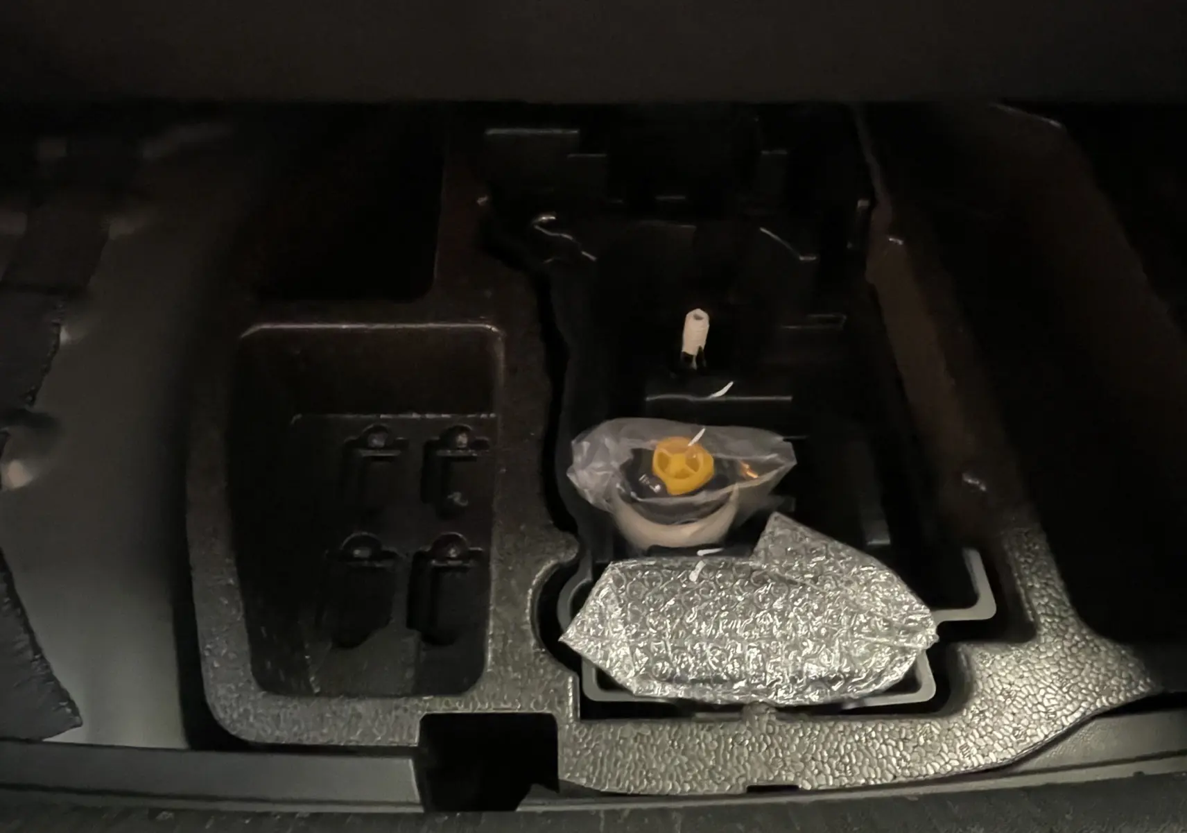 Compartiment de rangement sous le coffre d'une Peugeot 508 gris platinium, montrant des outils emballés et un espace vide.