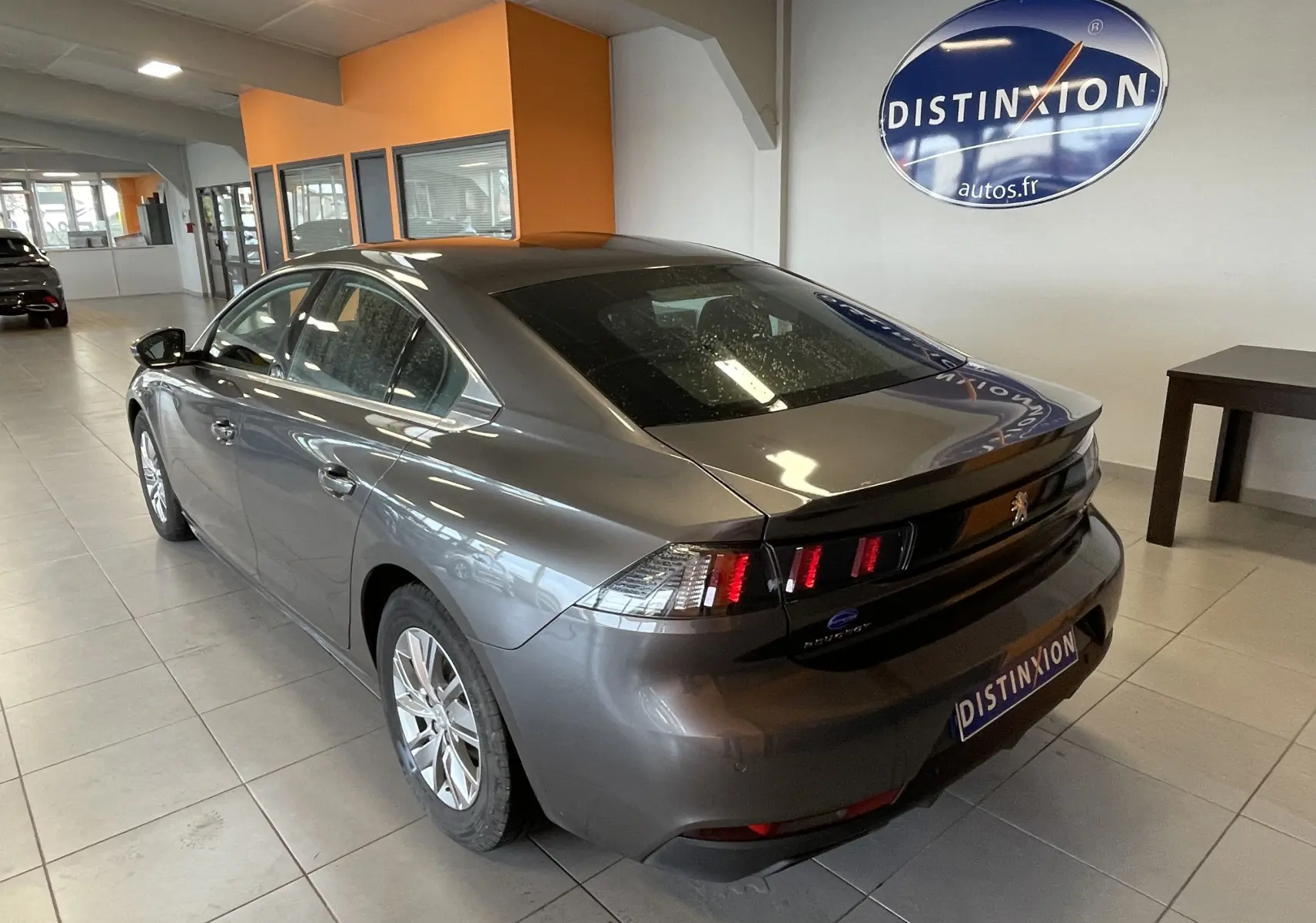 Vue 3/4 arrière droite d'une Peugeot 508 gris platinium dans un showroom avec logo Distinxion en arrière-plan.