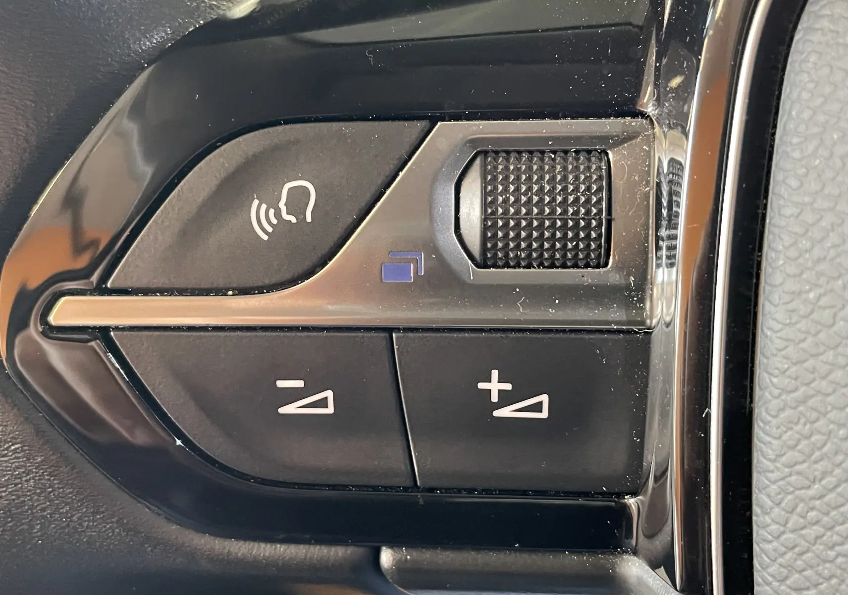 Gros plan sur les commandes au volant noir de la Peugeot 508 gris platinium, avec boutons de volume et activation vocale.