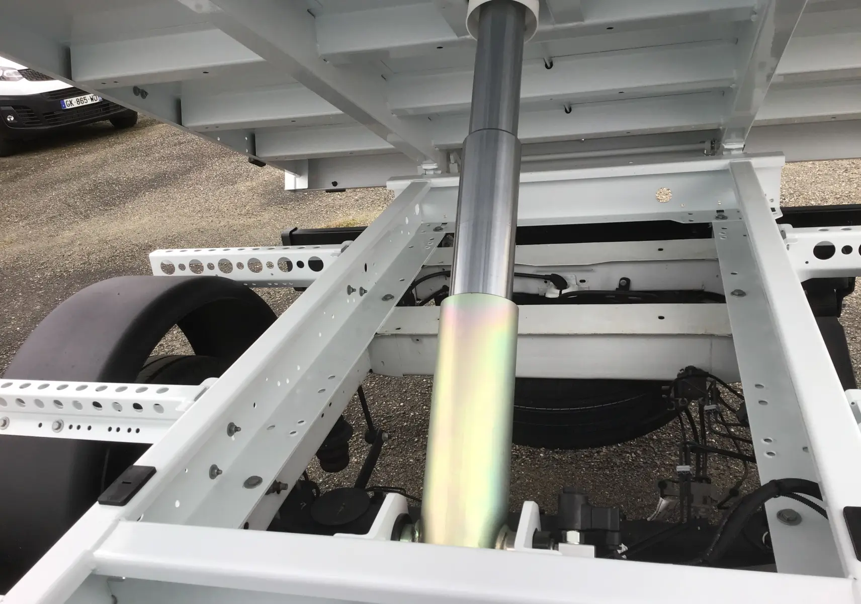 Gros plan sur le châssis blanc et le vérin hydraulique du Ford Transit Chassis Cabine benne blanche, vue arrière.