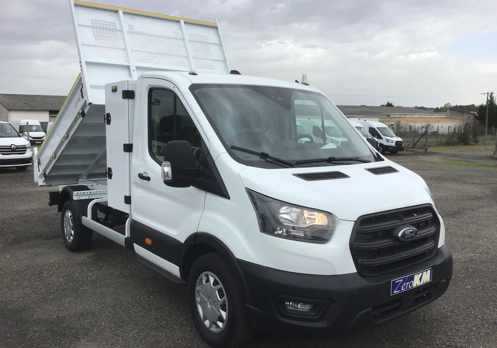 Ford Transit Chassis Cabine blanc en vue 3/4 avant droit avec benne relevée et coffre latéral acier.