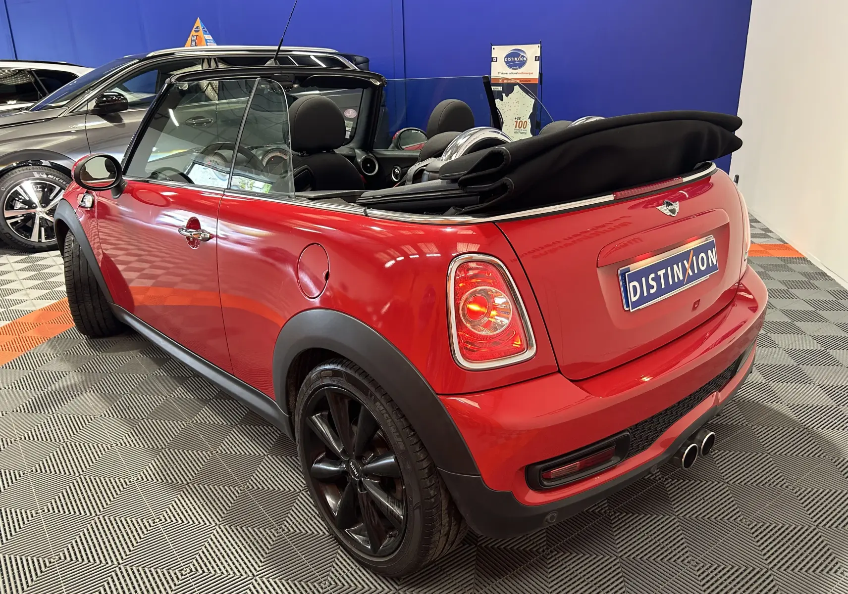 Vue arrière d'une MINI Cabriolet Cooper S rouge de 2012 avec capote noire repliée et double sortie d'échappement chromée.