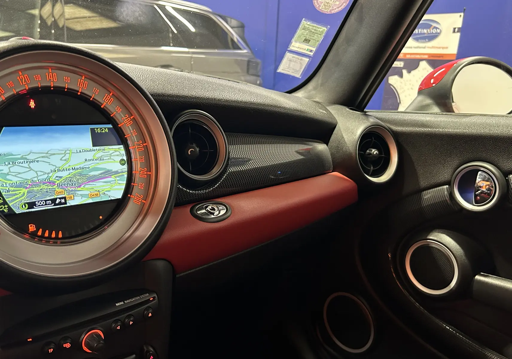 Vue intérieure côté passager du tableau de bord rouge et noir du MINI Cabriolet Cooper S 2012 avec écran GPS allumé.