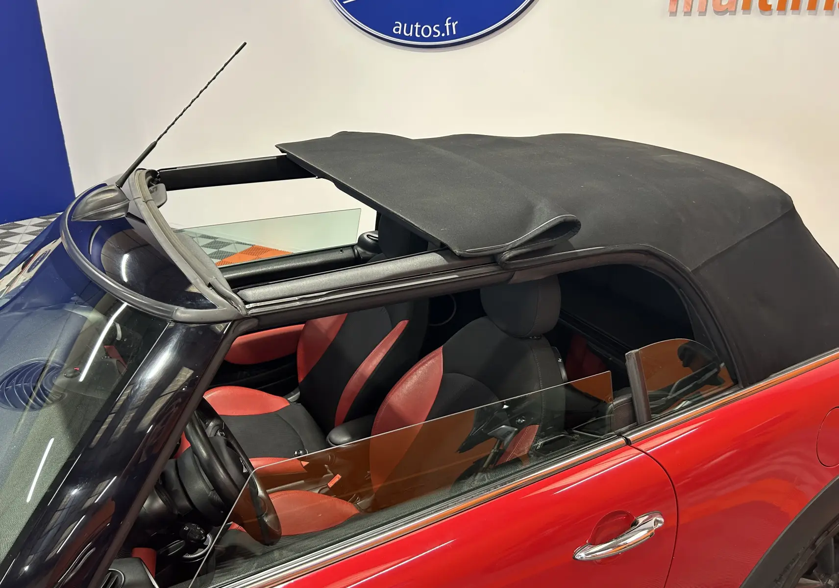 Vue 3/4 arrière d'une MINI Cabriolet Cooper S rouge avec capote noire fermée et jantes noires.