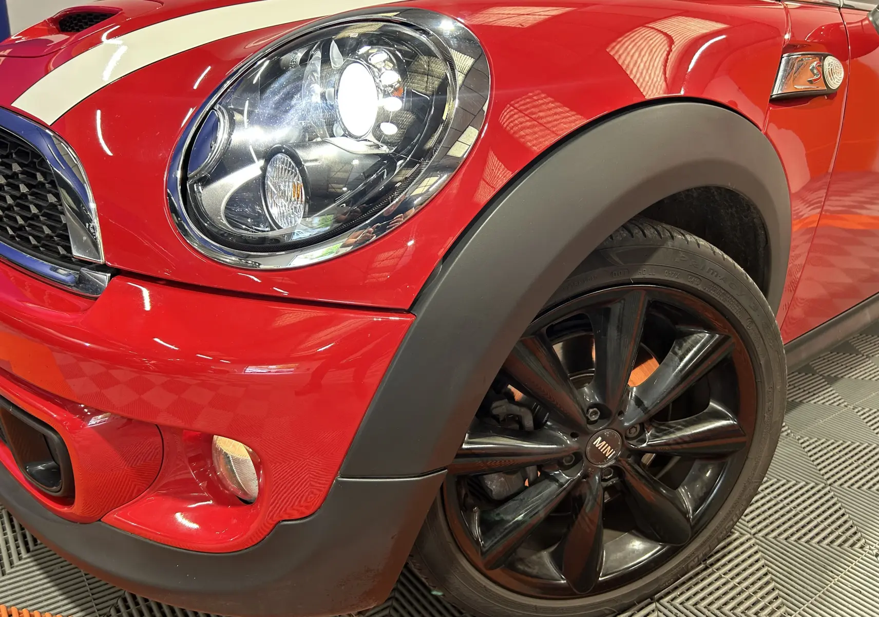 Gros plan sur l'avant droit rouge vif d'une MINI Cabriolet Cooper S 2012, avec phare allumé et jante noire brillante.