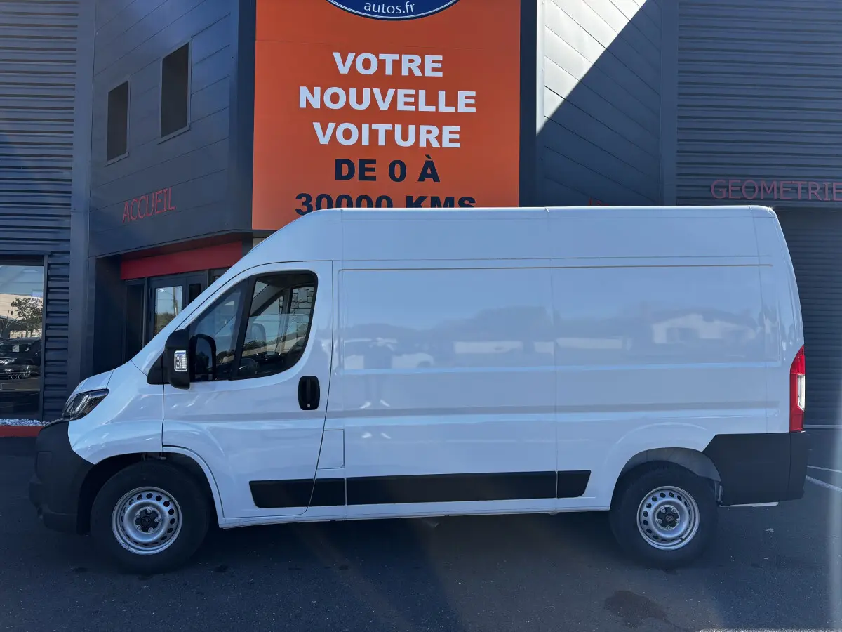 Fourgon Peugeot Boxer blanc vu de profil côté gauche, avec cloison pleine et jantes acier grises.