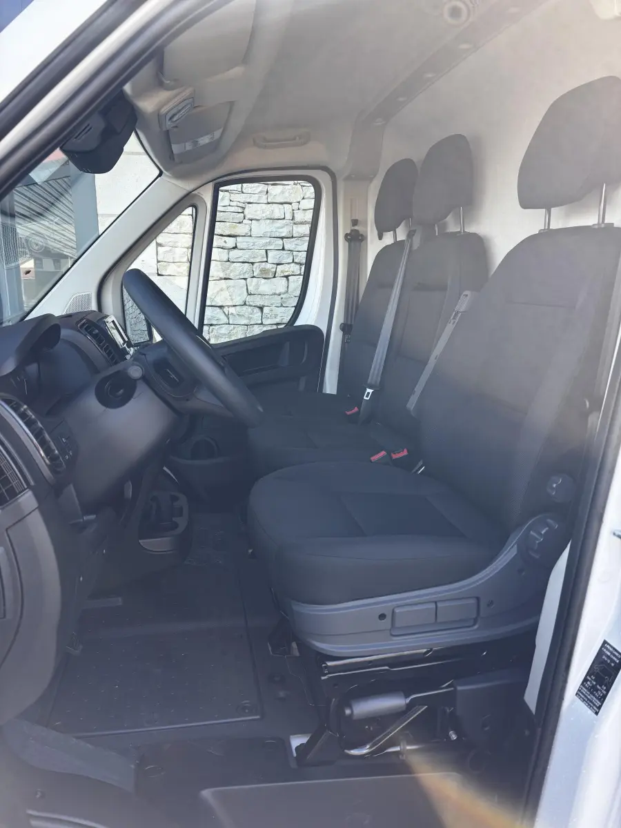 Vue intérieure côté conducteur du Peugeot Boxer Fourgon blanc 2025, montrant les sièges noirs et le tableau de bord.