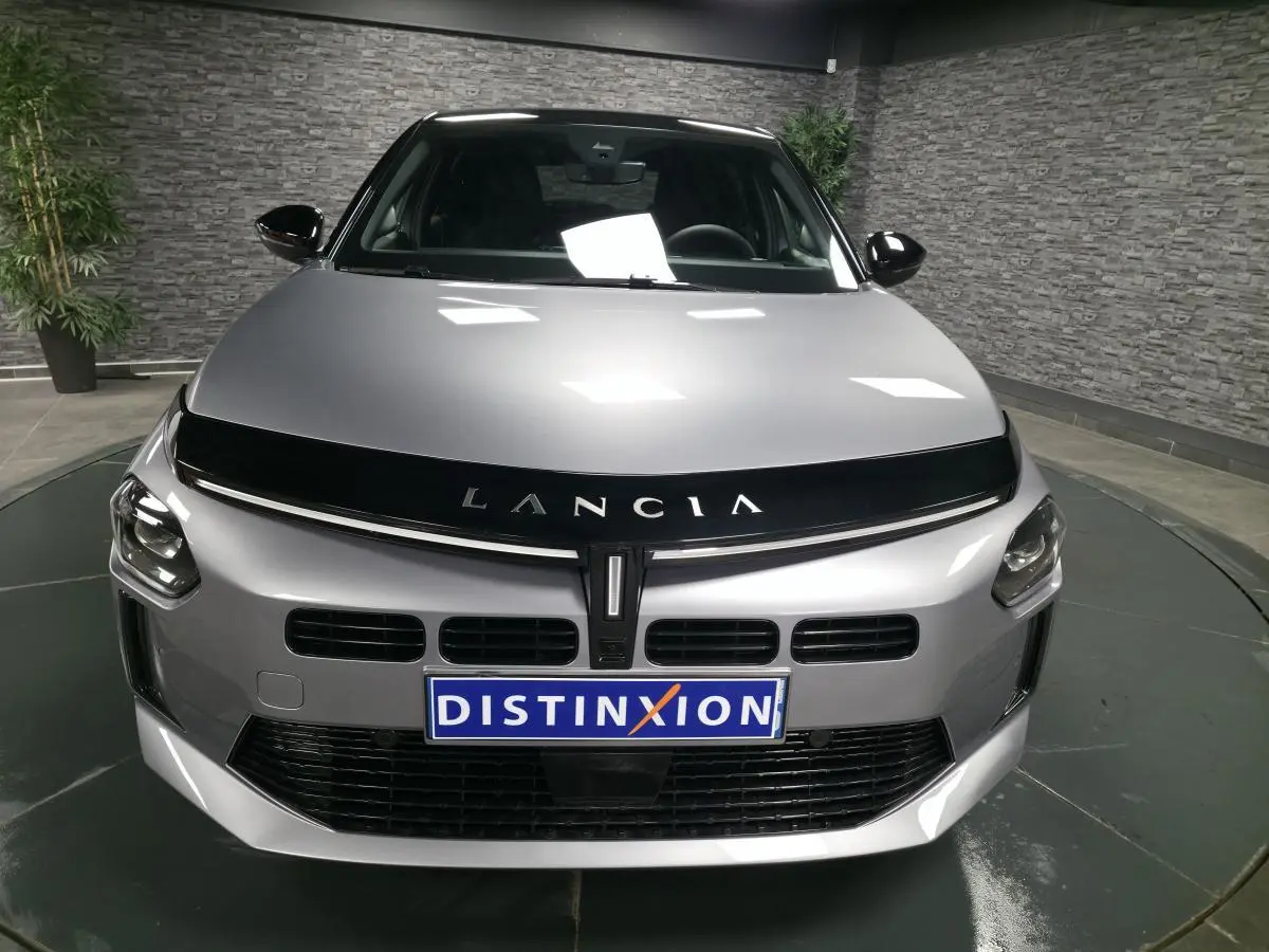 Vue frontale d'une Lancia Ypsilon 2025 gris métallisé avec calandre noire et logo Lancia bien visible.