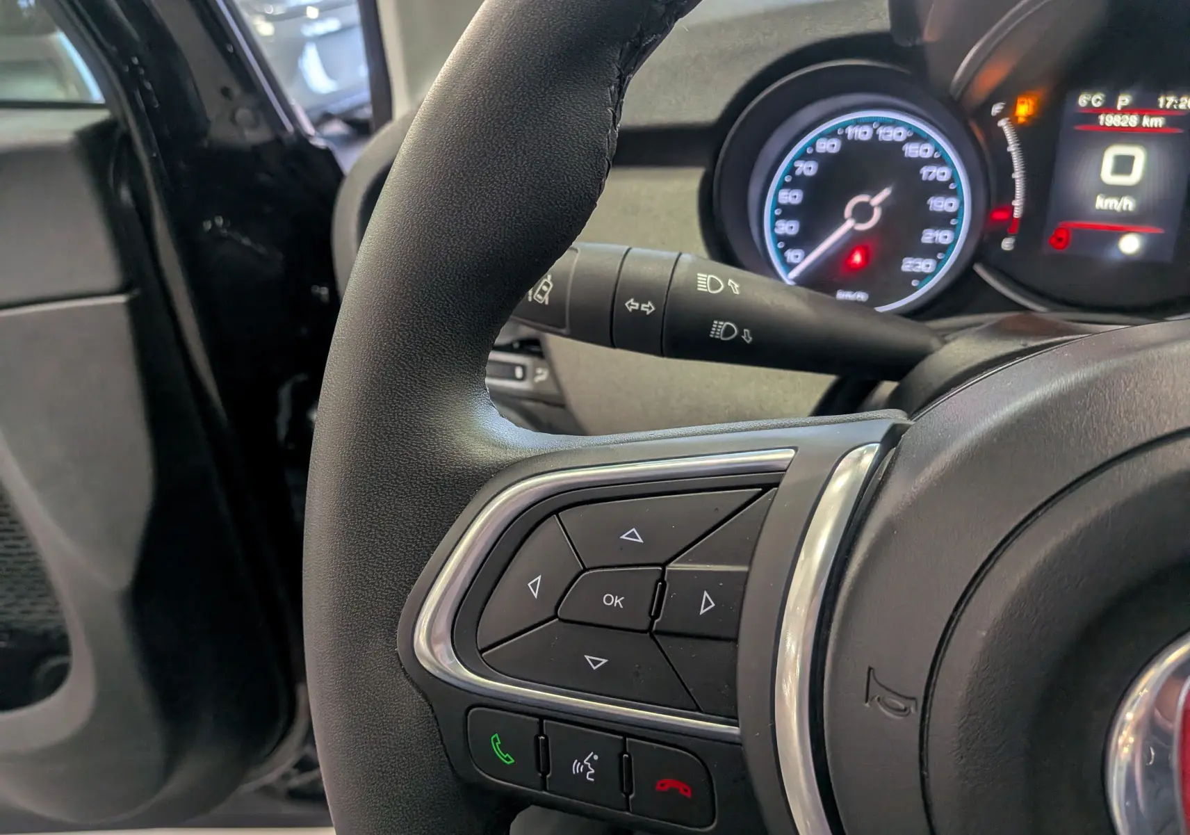 Gros plan sur le volant côté gauche du Fiat 500X 2024 noir, avec commandes intégrées et tableau de bord numérique en arrière-plan.