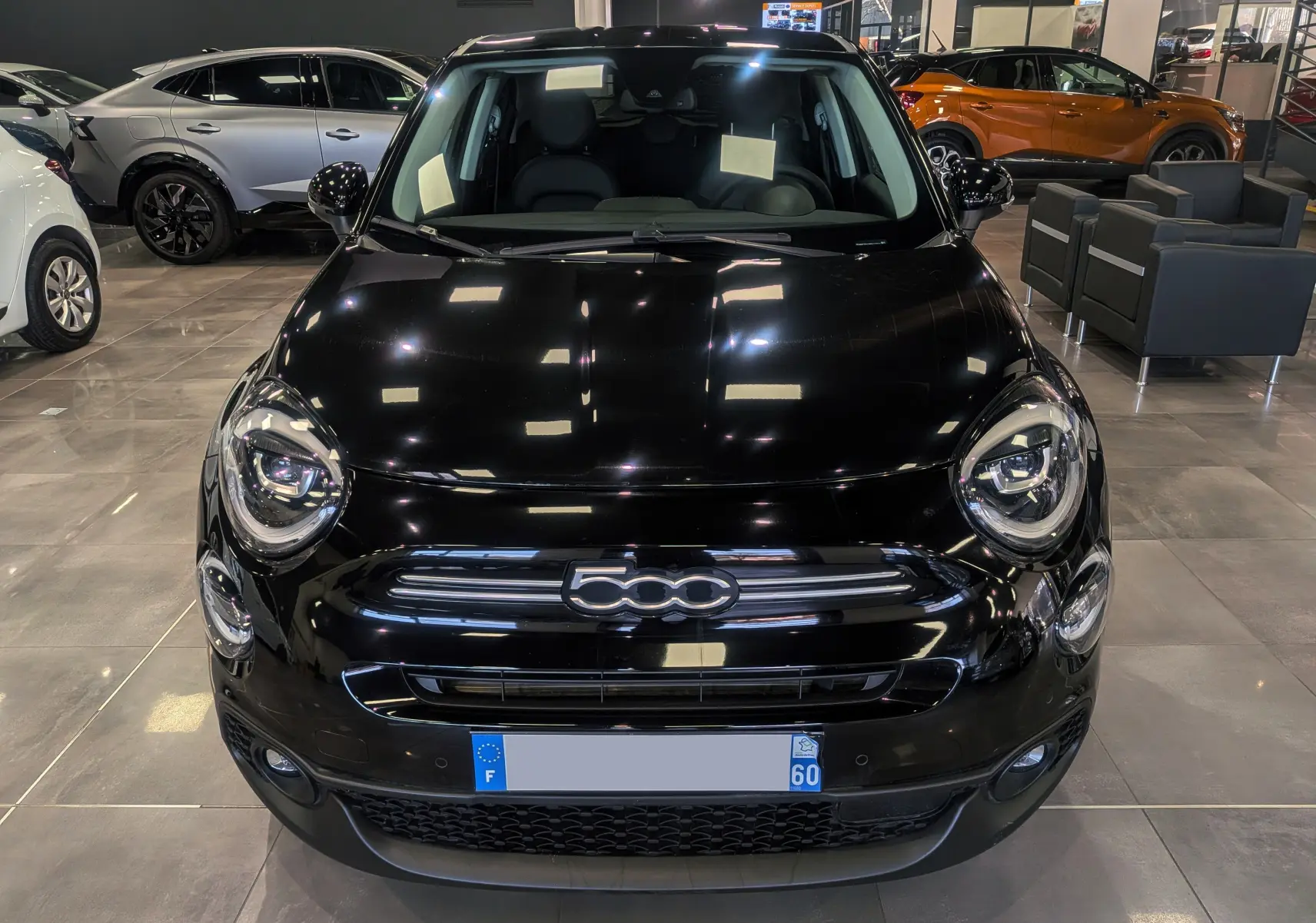 Vue frontale d'une FIAT 500X noire brillante exposée en showroom avec éclairage intérieur et sièges visibles.