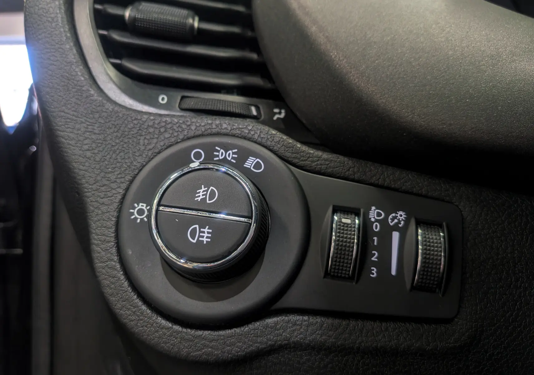 Détail du bouton de commande des feux et réglages d’éclairage sur le tableau de bord noir du Fiat 500X 2024.
