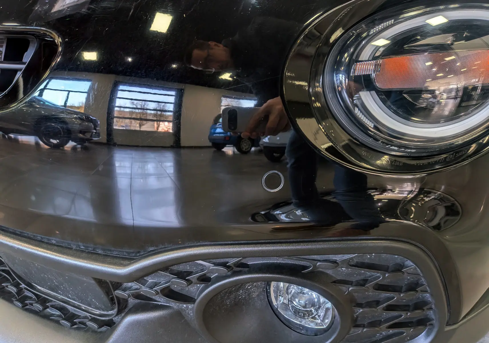 Gros plan sur le phare avant droit et la calandre d'une FIAT 500X 2024 en noir cinéma avec finition brillante.