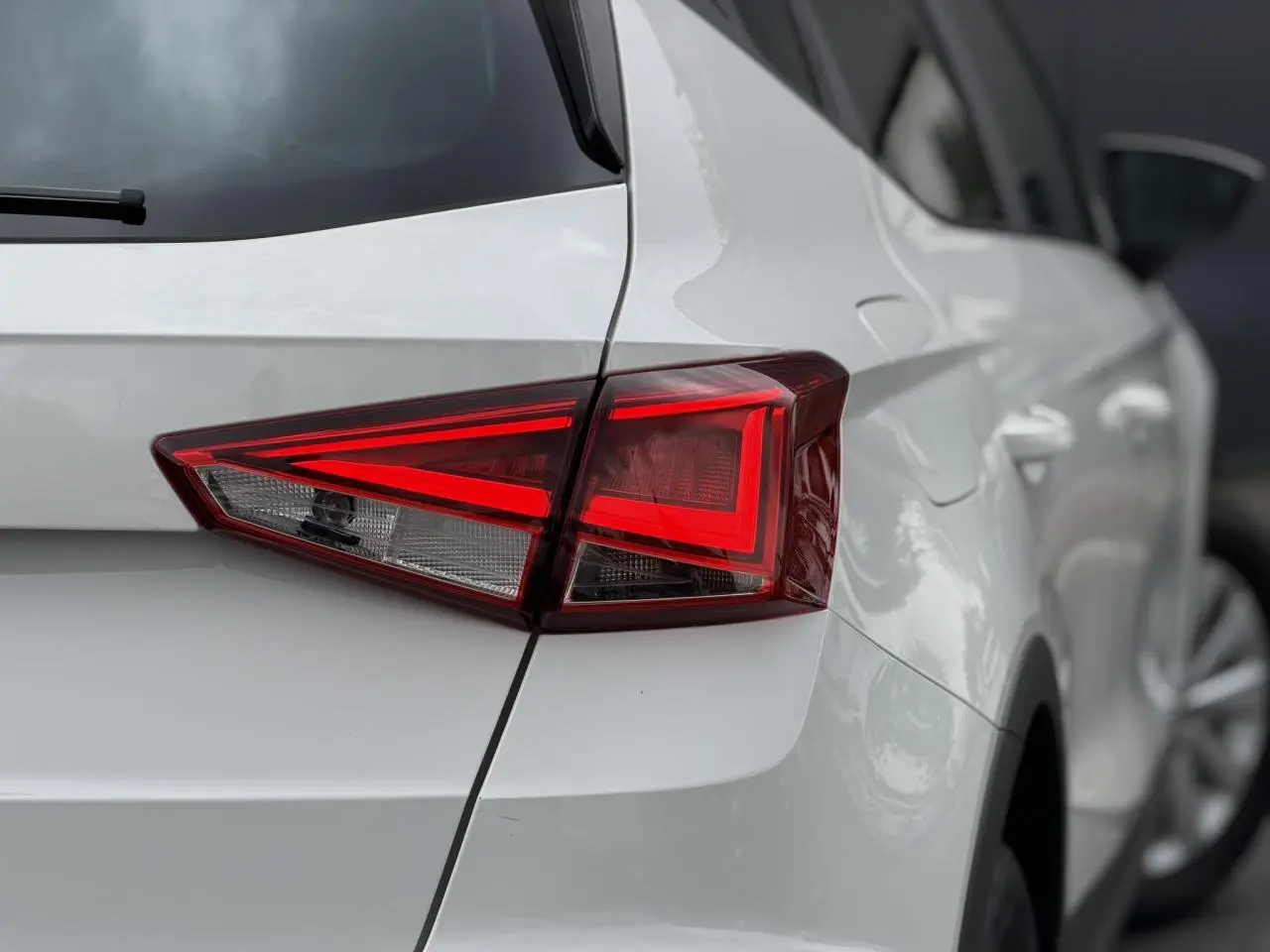 Gros plan sur le feu arrière droit d'un SEAT Arona blanc, mettant en valeur la ligne anguleuse et la carrosserie brillante.
