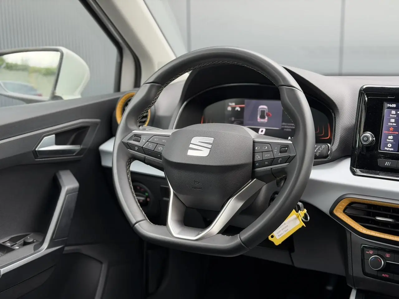 Vue intérieure centrée sur le volant noir du SEAT Arona blanc, avec tableau de bord digital et aérateurs orange.