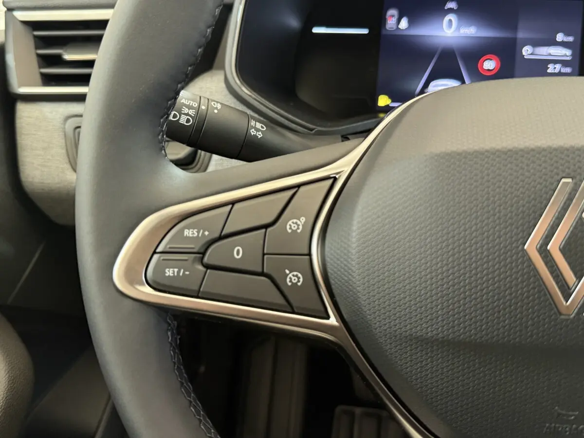 Gros plan sur le volant cuir synthétique de la Renault Clio 2025, avec commandes multifonctions et tableau de bord numérique en arrière-plan.