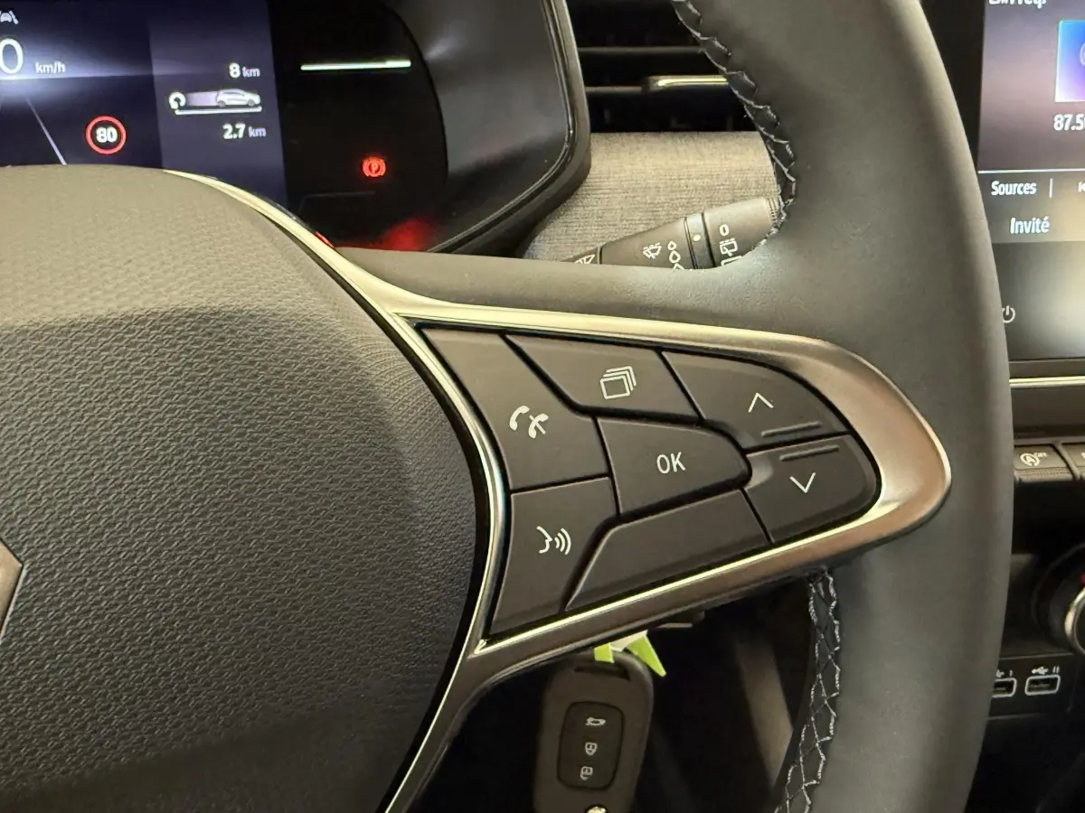 Gros plan sur le volant cuir noir de la Renault Clio 2025 avec commandes multifonctions et tableau de bord digital.